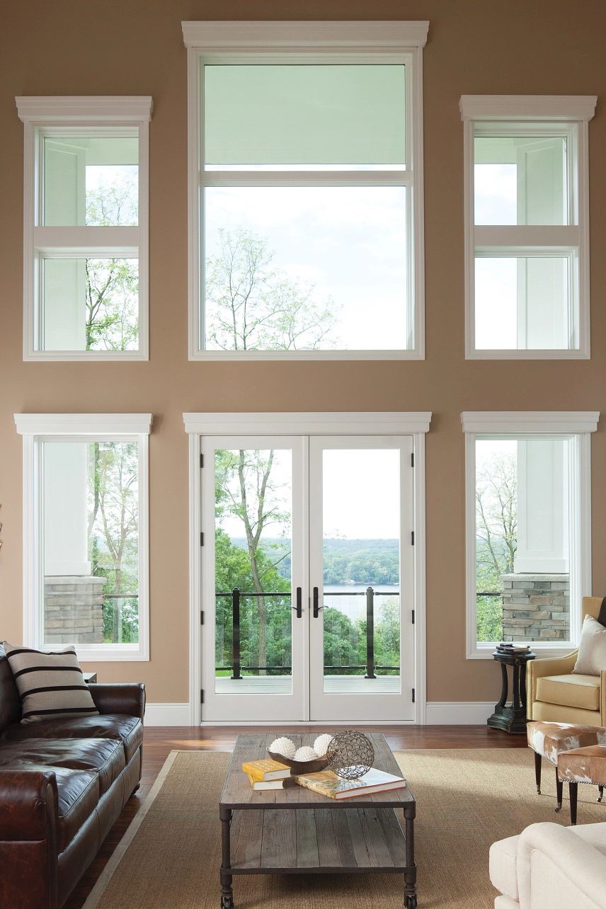 A living room with very tall ceilings, a patio door, and multiple picture windows.