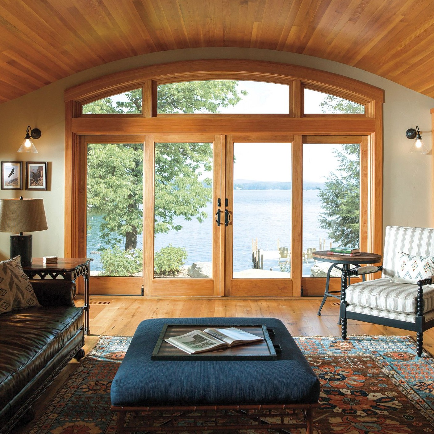 Two sets of sliding patio doors in a natural honey oak color. There is a custom set of arched transom windows above them and a view to a lake.