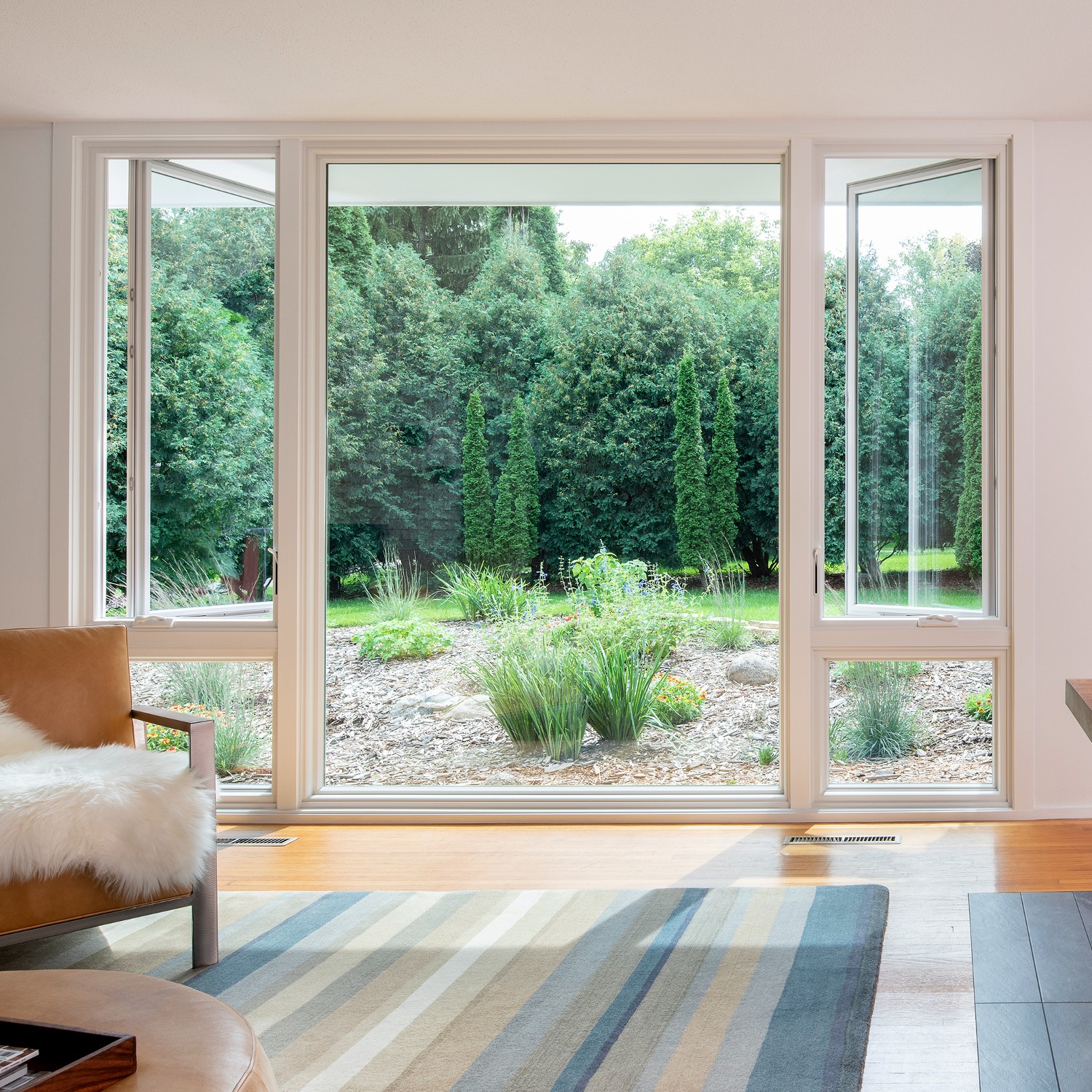 A mid-century modern style living room with an enormous picture window flanked by casement windows above smaller picture windows. The windows look out onto a garden.