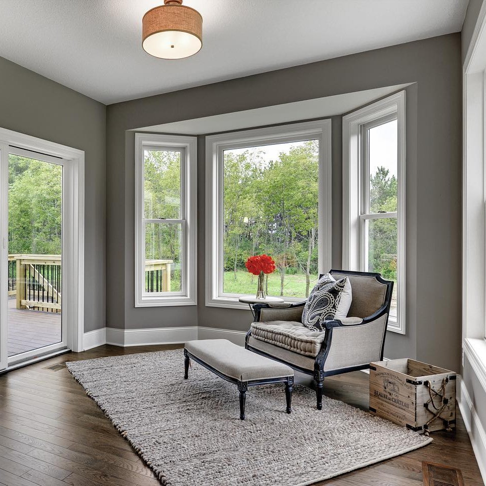 A dining room or reading nook with grey walls and a bumped out section that has a picture window facing the back yard.