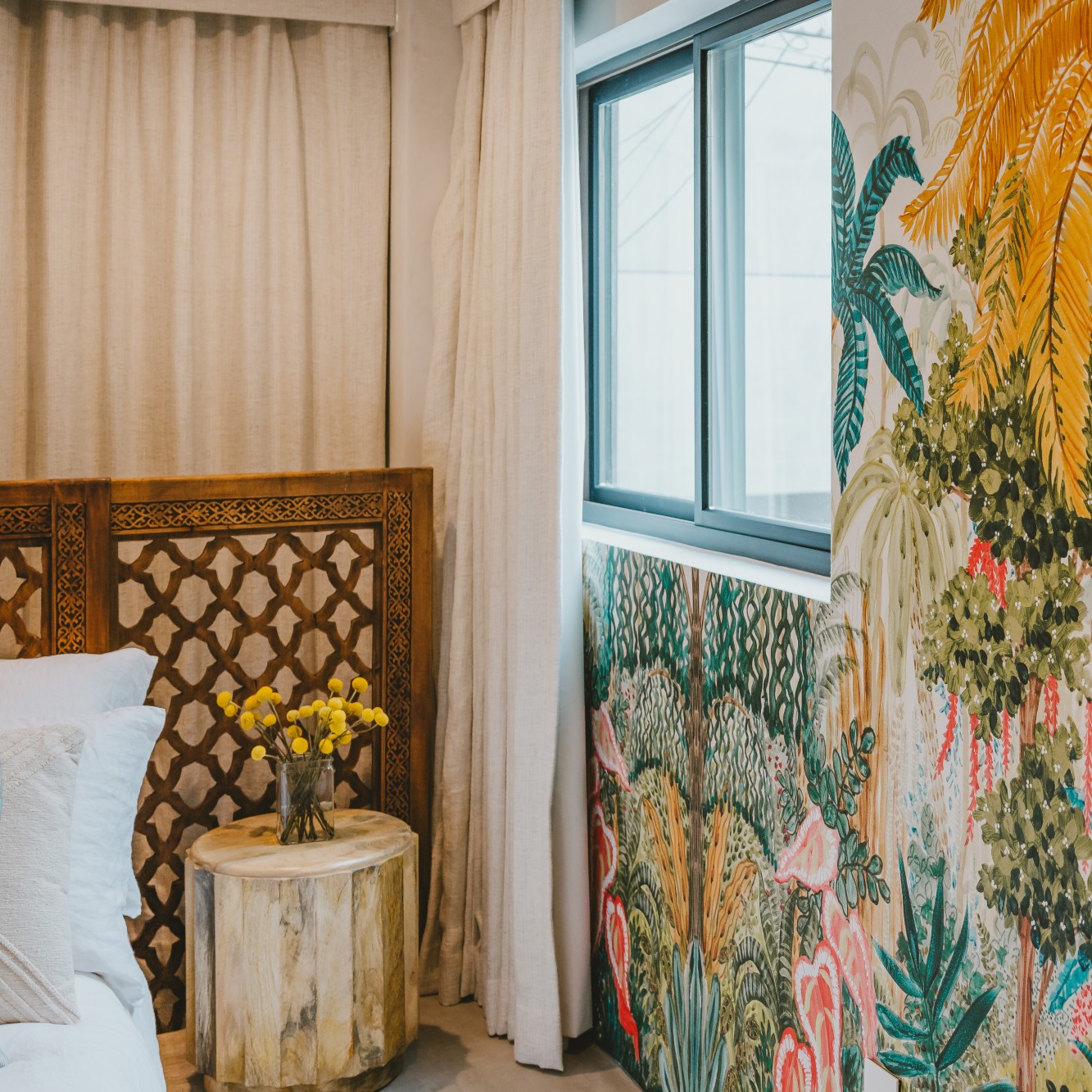A bedroom in Breegan Jane's home. There is a gliding window with a black frame and lots of tropical patterned wallpaper.